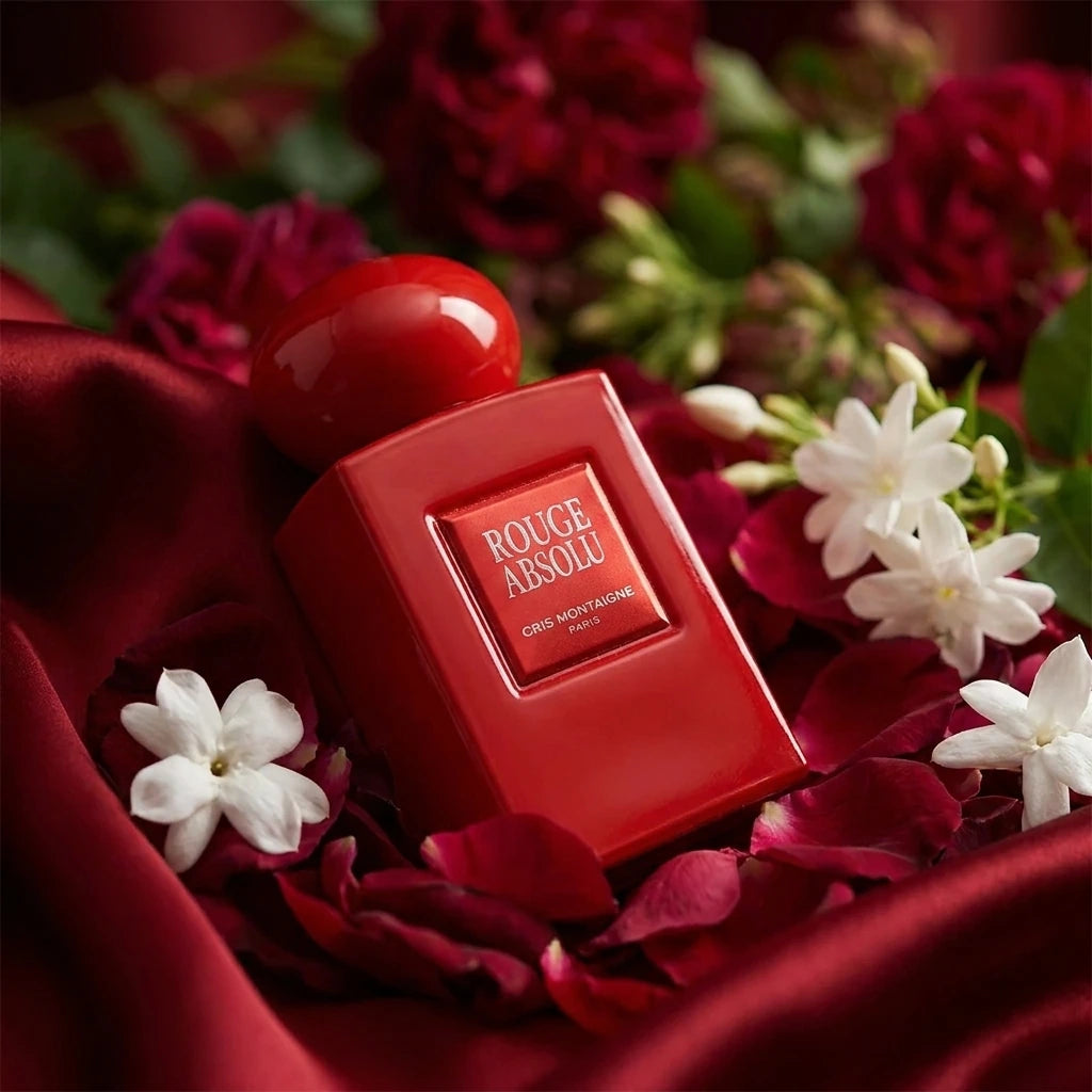 Concept de shooting : Une composition feutrée et théâtrale qui met en avant la volupté des fleurs de caractère. Le Prompt à copier : Une photographie de produit style nature morte organique et poétique. Le flacon rectangulaire rouge laqué brillant "ROUGE ABSOLU" est installé au creux d'un drapé fluide en soie rouge opulente. Le flacon émerge subtilement d'un lit dense de pétales de roses de Damas rouge sombre et de fleurs de jasmin blanc royal écloses. Une lumière diffuse et tamisée de style clair-obscur