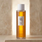 Premium commercial studio shot of the Beauty of Joseon Ginseng Essence Water bottle (referenced from image_464141.png). Front-facing view, perfectly centered and standing upright. Soft, warm professional studio lighting illuminates the product from behind, showcasing the glowing golden transparency of the ginseng liquid. High-end modern Korean skincare e-commerce branding style. Clean, minimalist, and deeply sophisticated. Aspect ratio 1:1, size 1200x1200px. (gemini-3.1-flash-image-preview)