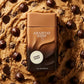 Une vue de dessus (flat-lay) artistique et gourmande sur un format carré de 1200x1200px. Au centre, le flacon de parfum bicolore "Arabiyat Sugar - Cookie Dough" de image_93c92b.jpg est posé à plat sur un lit dense de pâte à cookie brute, parsemée de grosses pépites de chocolat noir brillant et de morceaux de sucre roux cristallisé. L'éclairage studio est chaud et rasant, accentuant le fini mat du bouchon marron clair et la texture de la pâte environnante. (gemini-3-pro-image-preview)