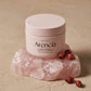 Angle : Prise de vue à $45^\circ$, légèrement surélevée pour donner du relief.Scène : Le pot d'Arencia de l'image image_c1c0dc.jpg est représenté fermé avec son couvercle rose poudré mat parfaitement vissé. Il est posé à la verticale sur un bloc asymétrique de quartz rose brut et cristallin. À côté du flacon, quelques baies de cynorrhodon (rosehip) séchées et ridées apportent une touche de texture authentique.Décor & Lumière : Fond de studio en stuc mat de couleur beige argileux doux. Une lumière latérale d