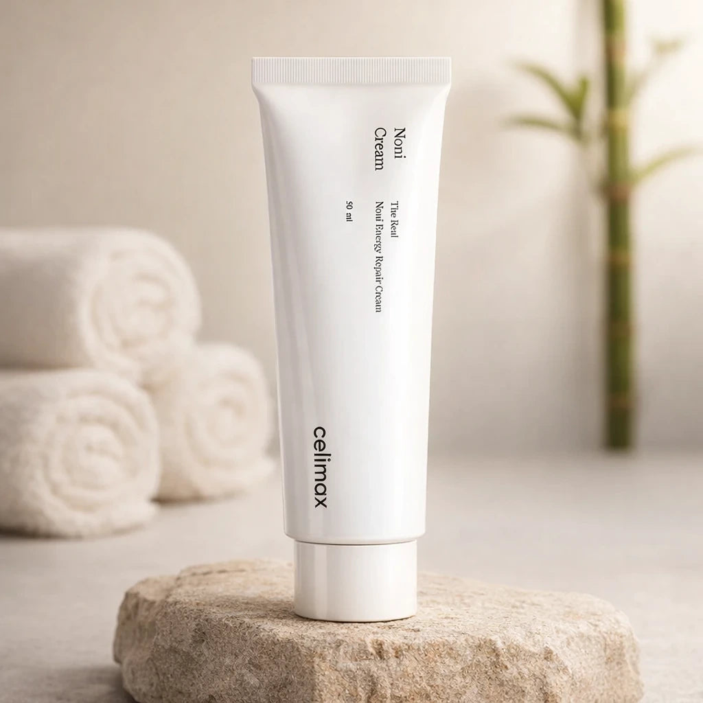 Premium spa product photography. A "Celimax Noni Energy Repair Cream" jar placed on a rough, textured raw stone block. In the blurred background, rolled white cotton towels and a subtle green bamboo stalk. Warm, relaxing diffused lighting, high-end wellness aesthetic, photorealistic --ar 1:1 (gpt-image-1.5)