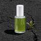 Commercial product shot, stark contrast style. The elegant 30ml glass bottle of Celimax Noni Energy Ampoule sits directly on rough, dark, deeply cracked asphalt pavement. The texture of the dry, damaged tar is highly detailed. A single, small green weed grows out of a nearby crack. Harsh midday sun creates strong, defined shadows, emphasizing the textures. The product remains clean and pristine against the urban decay. No special effects, raw realism. Shot on 70mm lens, F7 aperture, ISO 250. 8k resolution. 