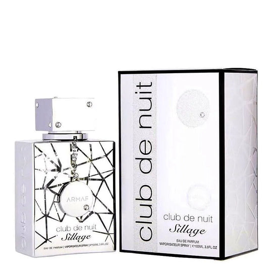 Eine schlanke, moderne Flasche von Armaf Club de Nuit Sillage Eau de Parfum Mixte, die eine silberne Kappe und ein abgestuftes blaues Glasdesign aufweist, das auf einem minimalistischen Hintergrund ruht.